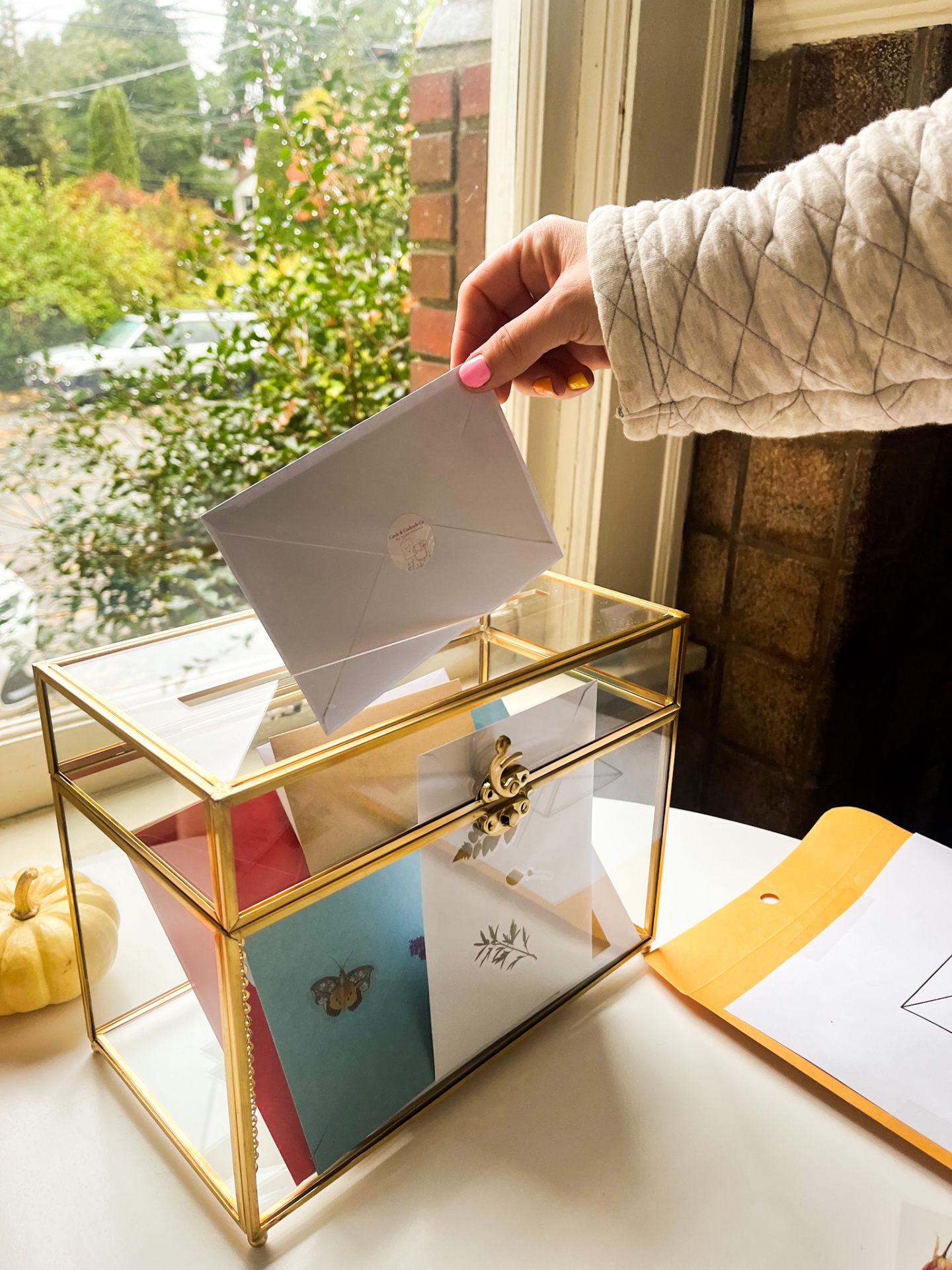 A handwritten card being placed in a glass and gold keepsake box